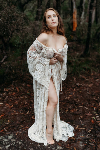 Woman wearing Mama Rentals Elvira Crochet Robe off the shoulder standing in a forest.