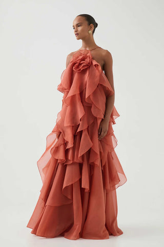 Woman wearing the Aje Pandorea Layered Maxi Dress in Coral Clay with halter neckline and voluminous ruffled layers, floor-length silhouette.