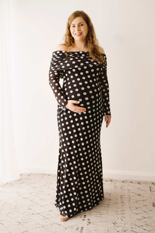 A pregnant lady wearing the Mama Rentals AFRM Thelma Off Shoulder Mesh Maxi Dress - Black in a studio.