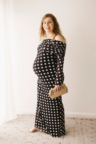 A pregnant lady wearing the Mama Rentals AFRM Thelma Off Shoulder Mesh Maxi Dress - Black in a studio.