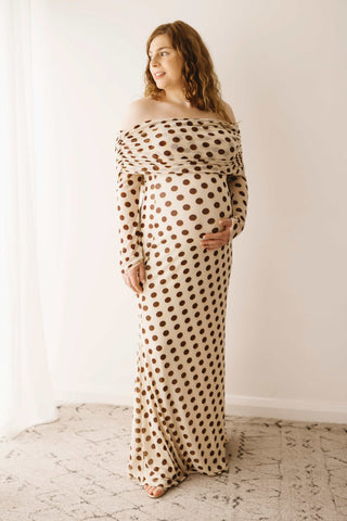 A pregnant lady wearing the Mama Rentals AFRM Thelma Off Shoulder Mesh Maxi Dress in Gold in a studio.