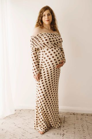 A pregnant lady wearing the Mama Rentals AFRM Thelma Off Shoulder Mesh Maxi Dress in Gold in a studio.