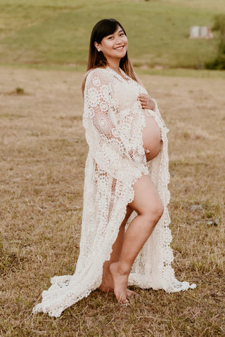 Pregnant woman in a lace dress, the Mama Rentals Elvira Crochet Rob standing in a field for her maternity shoot. 