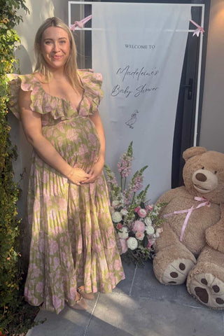 Woman in a Zimmermann Lovestruck floral dress standing next to a teddy bear and floral arrangement at her baby shower