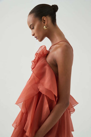 Back view of woman wearing the Aje Pandorea Layered Maxi Dress in Coral Clay with open back, tie straps, and cascading ruffle layers.