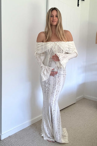 Woman wearing the Mama Rentals House of CB Belle Vintage Cream Floral Lace Off Shoulder Maxi Dress in a room with a plain white wall.
