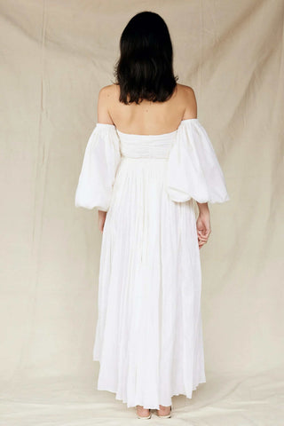 Woman wearing a Rooh Collective white off-shoulder dress against a beige background