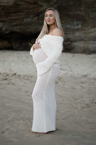 A pregnant lady in a beach wearing the Meshki Marisol Off Shoulder Boucle Maxi Dress at her maternity photoshoot.

