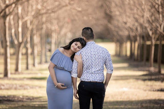 A beautiful pregnant lady wears Mama Rentals Isabel Off the shoulder ruffle maternity dress in dusty blue at her maternity shoot with her partner.
